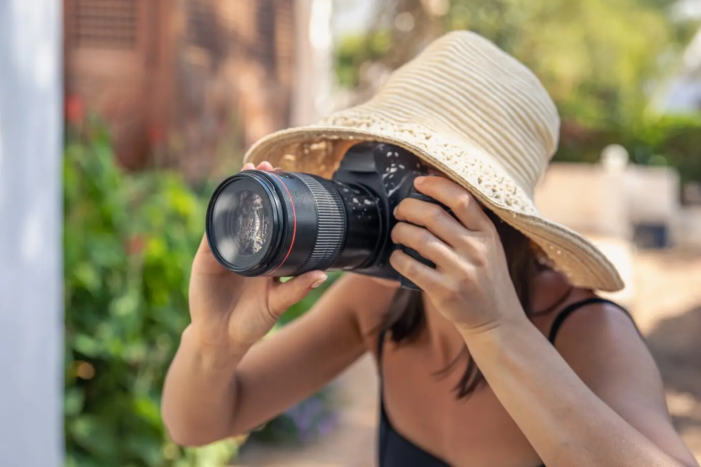 Eine junge Frau mit Hut fotografiert an einem heißen Sommertag mit einer professionellen Spiegelreflexkamera.