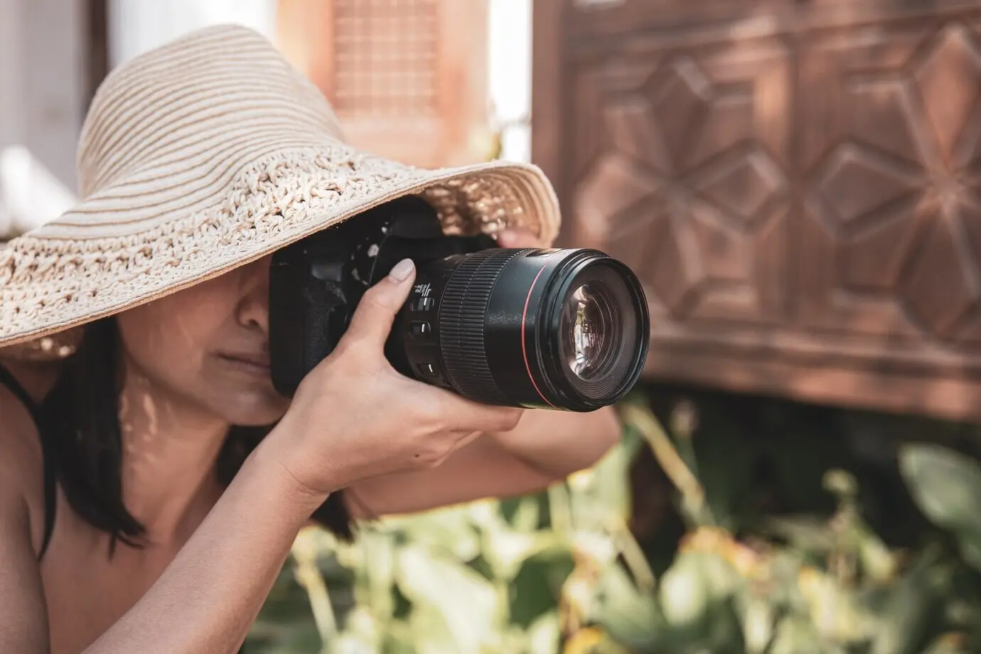 Eine junge Frau mit Hut fotografiert an einem heißen Sommertag mit einer professionellen Spiegelreflexkamera.